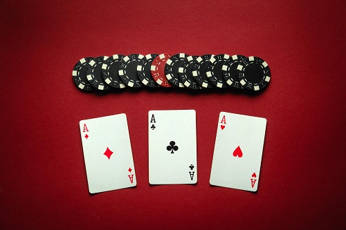 Three ace playing cards with playing chips above them all put on a red table